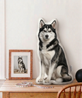 Husky-shaped pillow on a wooden table with a framed photo and cat in the background